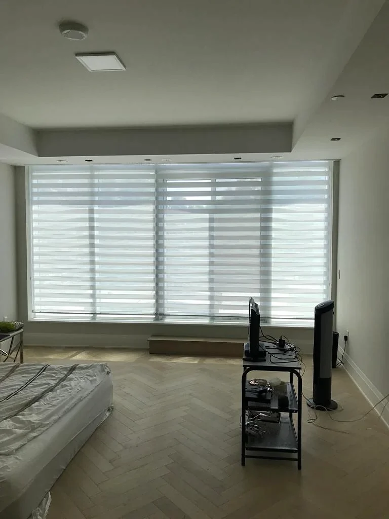 A bedroom with full-height windows and one zebra shade across them