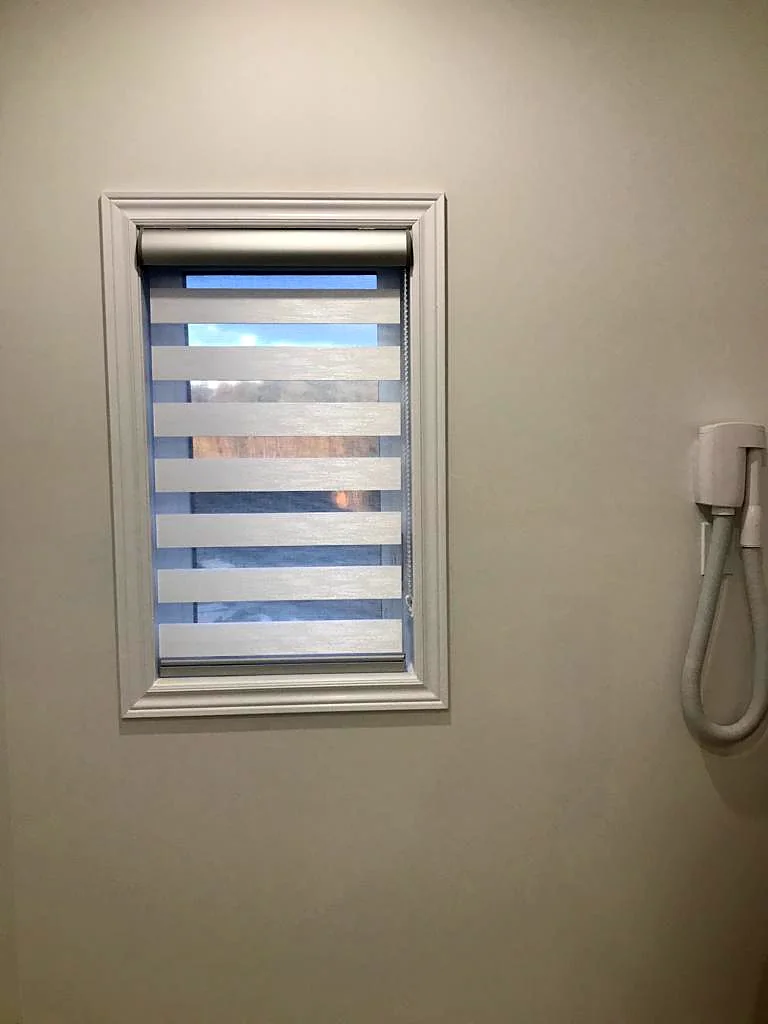 A small bathroom window with a zebra shade inside its frame